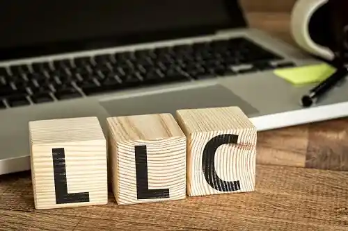 Wooden blocks spelling LLC on a desk next to a laptop